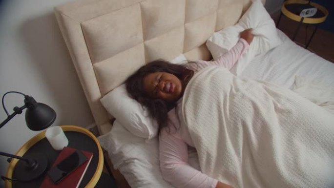 睡觉的女性在床上用枕头遮住耳朵