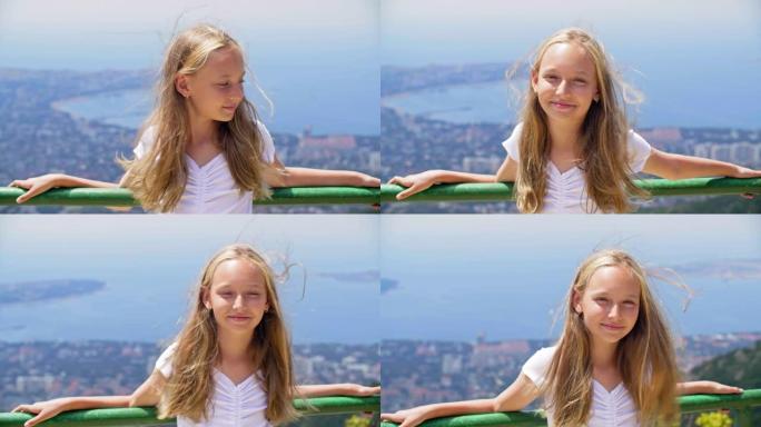 微笑的女孩少年，头发在风中站在山顶的观景台上，拿着栏杆。海湾景观山峰上的快乐旅游女孩。