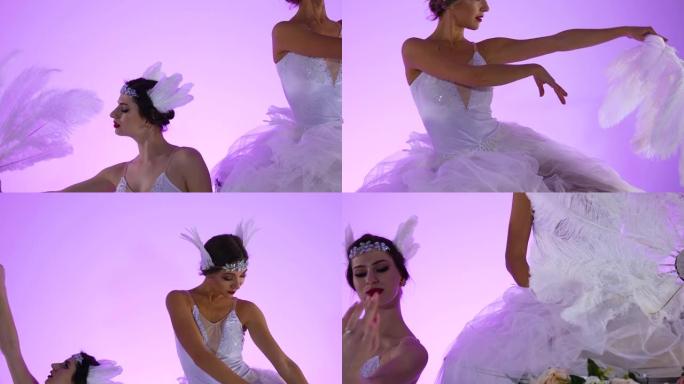 穿着白色天鹅服装的精致女性芭蕾舞演员在装饰有花朵的蛋糕上摆姿势。两名年轻女性在工作室的粉红色背景上优