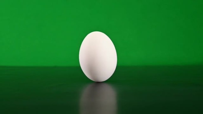用手扭曲一个白色的鸡蛋，然后在chromakey背景上的深色硬表面上进行旋转。