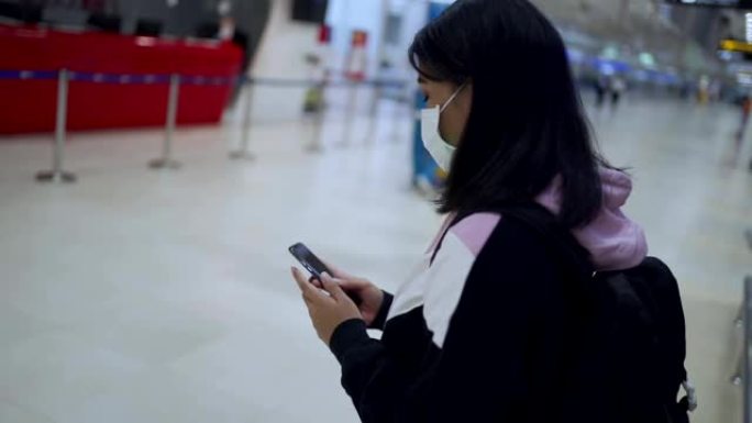 亚洲女性在机场航站楼主厅使用智能手机佩戴医用口罩，旅行导航系统应用，病毒新型冠状病毒肺炎大流行后，新