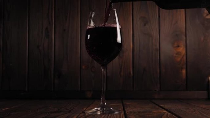 将红酒倒入木制背景的玻璃杯中。慢动作。