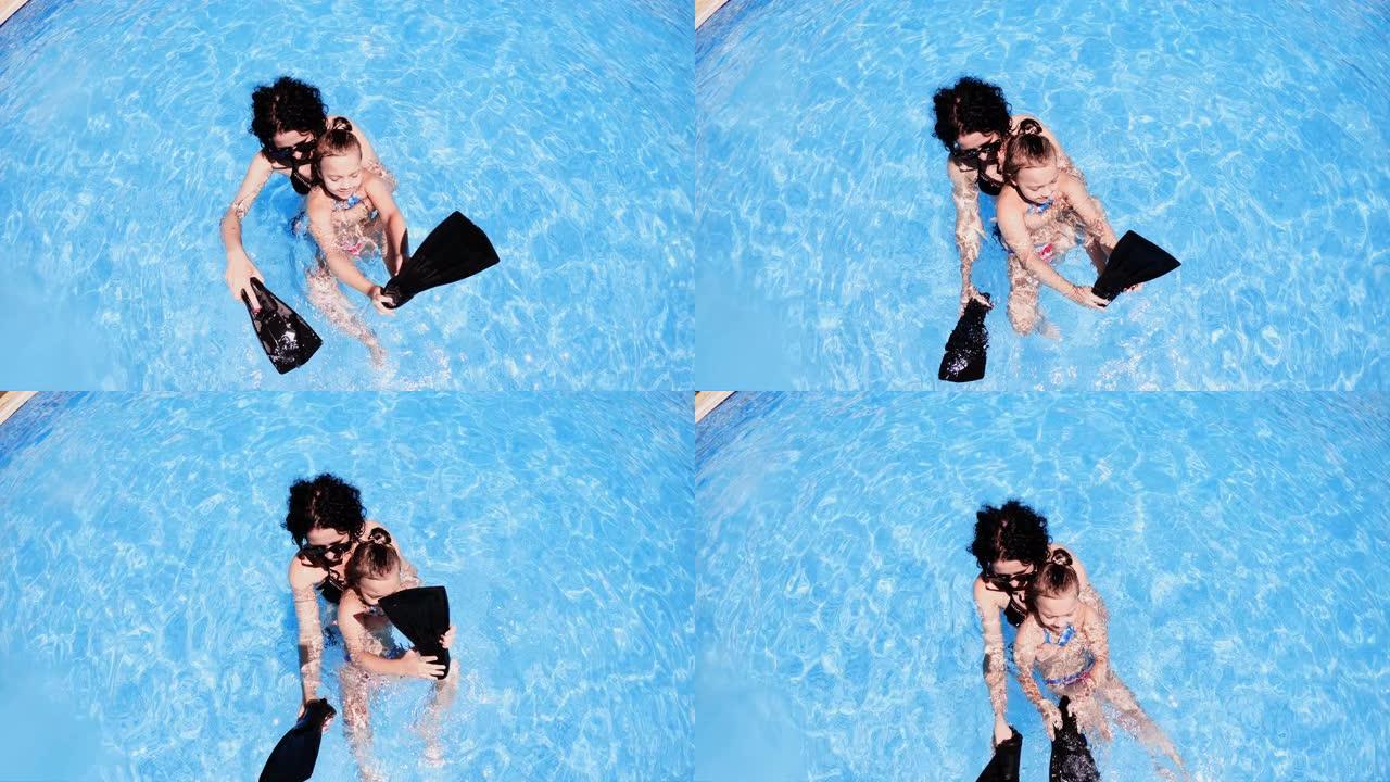 年轻开朗的母亲在暑假在游泳池里给她的小女儿上游泳课