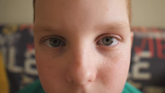 绝望的红发小男孩带着雀斑看着室内相机的肖像。特写悲伤孩子的男性脸。绝望的姜小子坐在沙发上。小家伙失望