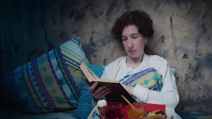 成熟的女人在床上吃早餐时看书