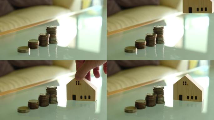 室内拍摄，有选择性的聚焦在男人手把木房子模拟在增加一叠硬币旁边。储蓄，赚钱买房的概念。成功时刻。