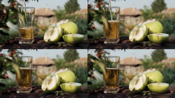将青苹果汁倒入玻璃杯中。在乡间别墅和大自然的背景下，将青苹果汁倒入透明玻璃中，附近有新鲜的青苹果。特