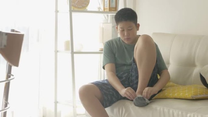 亚洲男孩早上在家穿着袜子在沙发上靠近窗户，生活方式概念。