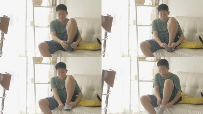 亚洲男孩早上在家穿着袜子在沙发上靠近窗户，生活方式概念。