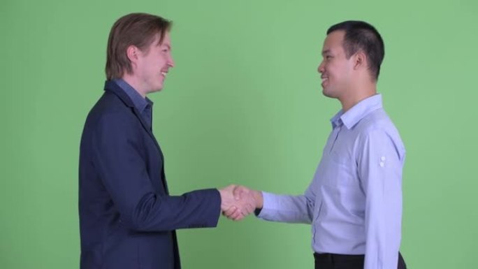 两个商人在绿色工作室背景下微笑时握手