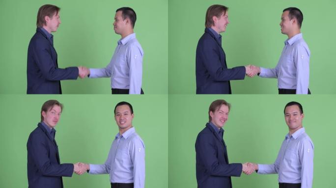 两个商人在绿色工作室背景下微笑时握手