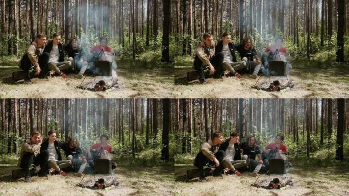 男人们坐在树林里的火炉旁。他们在徒步旅行时弹吉他。他们快乐地唱歌。有趣就是有趣。自然界中积极的生活方