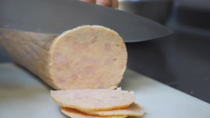 在烹饪时，用小刀将男性的手在塑料砧板上切成香肠片。厨师在厨房餐厅准备烹饪披萨的配料。慢动作