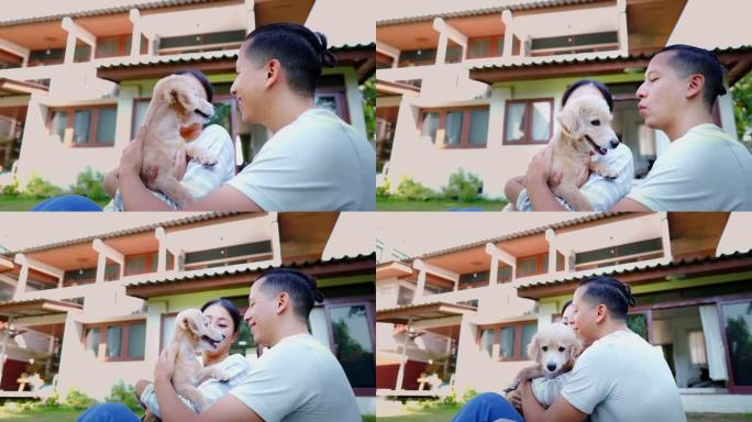年轻的亚洲成年夫妇抱着一只背景为家庭内部的小狗。30多岁的成熟男人在花园里抱着一只狗宠物。夫妻一起住