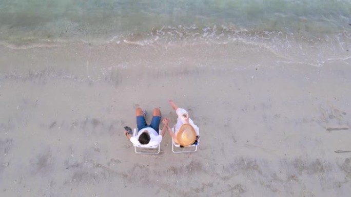情侣手牵着手坐在沙滩上的晒黑椅子上
