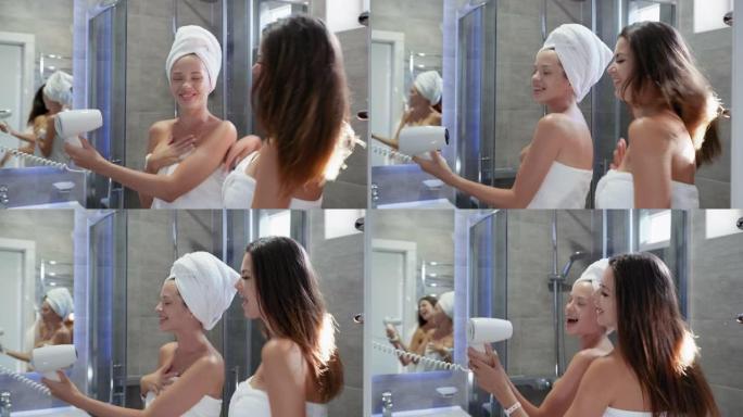 生活方式，穿着毛巾的迷人年轻女性在淋浴时玩得很开心，对着吹风机唱歌，就像对着麦克风在浴室里笑着唱歌