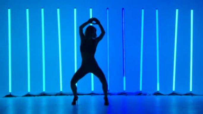 苗条的舞者通过慢动作优雅地移动臀部来练习莎莎舞的动作。在明亮的蓝色霓虹灯的背景下，工作室中女人的剪影