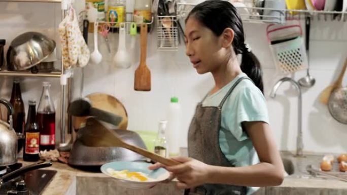 快乐的亚洲女孩在家里的厨房里穿着围裙和烹饪煎蛋，生活方式的概念。
