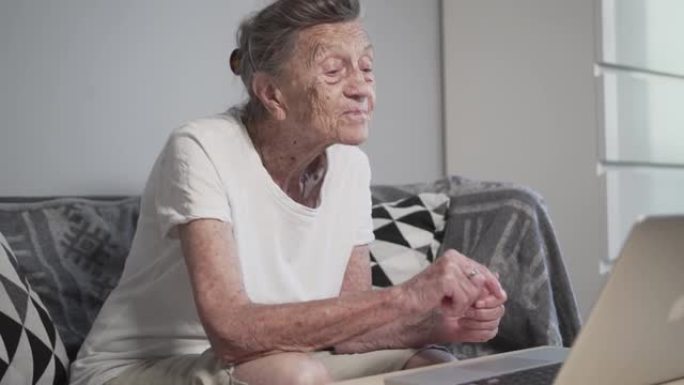 老年妇女与家人进行视频通话，微笑着挥手。头发花白的高级女性在家使用笔记本电脑进行视频通话。新型冠状病