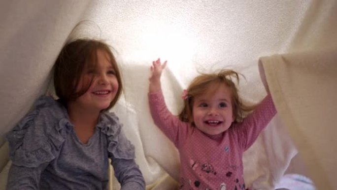 爱玩的快乐的姐妹们在她们做的床单堡垒下玩耍