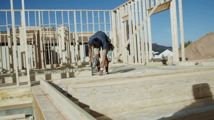 年轻的木匠建筑工人使用气动钉枪将木框墙放在一起，以在建筑工地上建造的住宅中垂直抬高