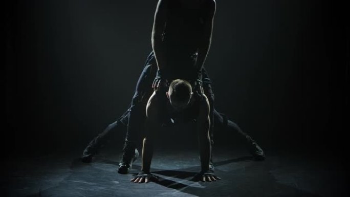 男性体操运动员表演复杂的杂技特技。一名体操运动员进行倒立，而另一名体操运动员则在空中保持平衡。慢动作