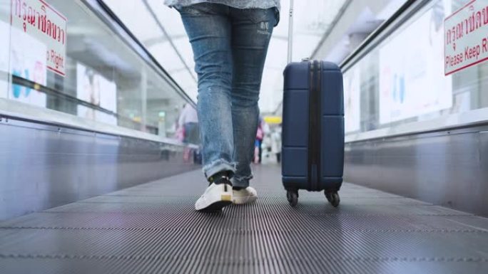 在机场的自动扶梯步行路上低头看着带着手提箱的旅行者