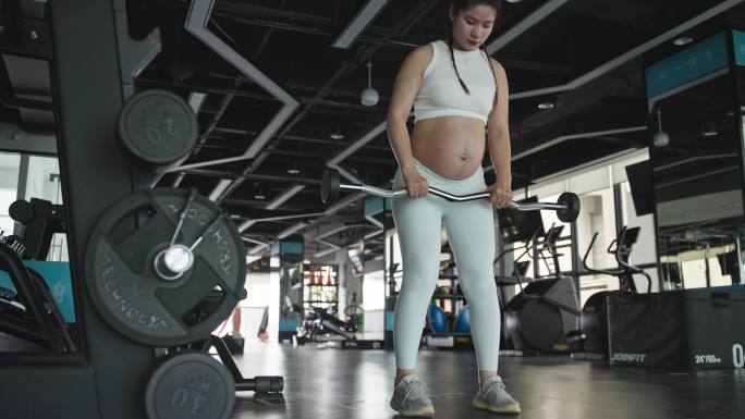 怀孕的现代女性在健身房锻炼身体举杠铃撸铁