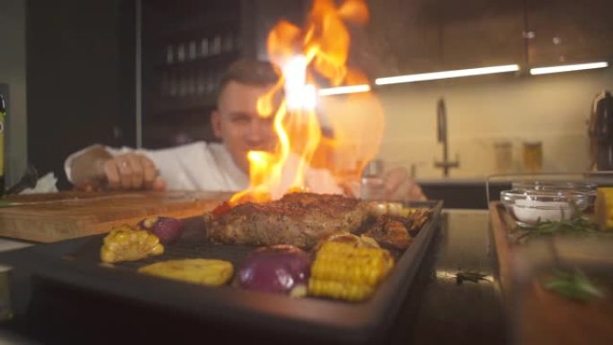厨师看烧烤现代厨房的肉牛排特写。用火餐厅准备火焰烤盘。烤架煎锅里的火焰。做美味的食物。在菜肴上加工餐