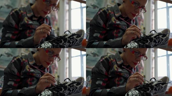 迷人的女艺术家在她的工作室中以有趣的方式画运动鞋