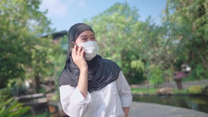 东南亚穆斯林女性戴防护面罩。头巾妇女在公园内散步时接听电话，打电话，冠状病毒新型冠状病毒肺炎伊斯兰国