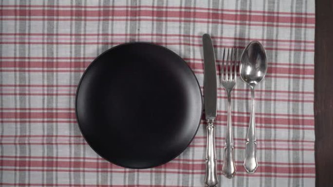 带餐巾和餐具的空黑色盘子。抽象食品背景。