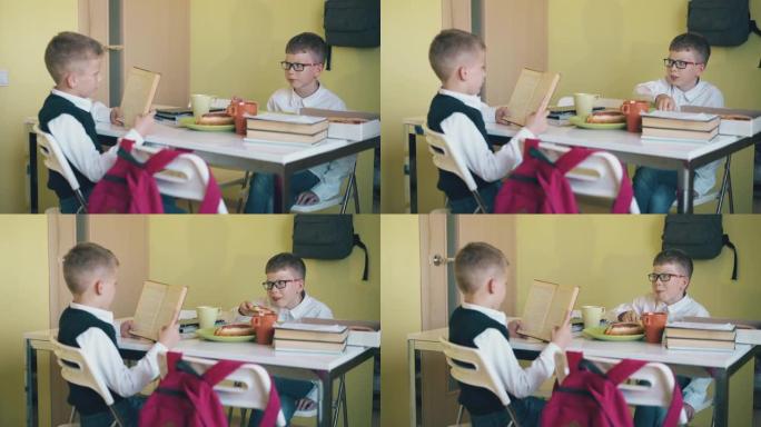 小学生向在食堂餐桌上吃饭的朋友读书
