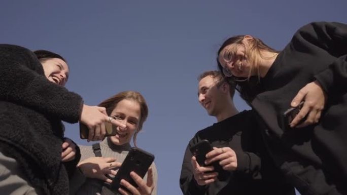 低角度的一群朋友使用智能手机并大笑。他在手机上教他们一些有趣的东西。新型冠状病毒肺炎季节新的正常生活