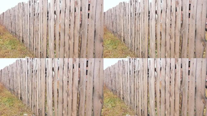 高高的木栅栏的特写镜头，前面长着草。乡村牧场的木制树篱。该领土被一个大的木栅栏包围。选择性聚焦