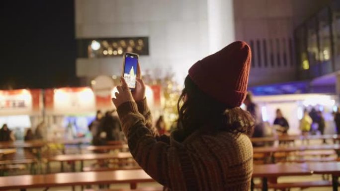 女人在圣诞市场用手机给圣诞树拍照。