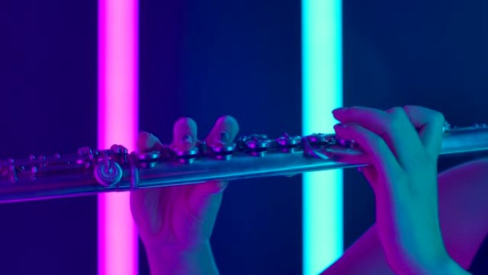 由专业长笛演奏家演奏的古典音乐交响音乐会。女性手触摸长笛的按键特写。明亮的紫色霓虹灯背景下的管乐器。