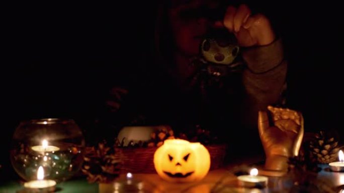万圣节，戴着兜帽的怪异男孩在黑暗的房间里用蜡烛和蜘蛛玩耍