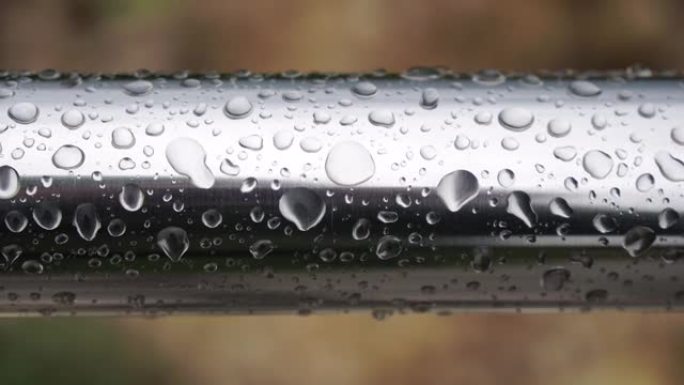 在模糊的海洋背景下，不锈钢扶手上的雨滴。特写镜头。雨露中的水滴聚集在闪亮的钢铬杆手轨栏杆上