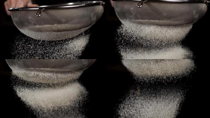 白色面粉的特写镜头从黑色背景上的钢筛中掉落