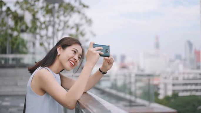 屋顶酒吧里美丽的亚洲女孩博主在曼谷泰国城市的背景下拍摄一张自拍照片，并上传到社交媒体