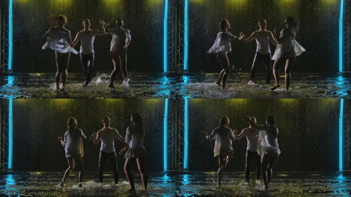 剪影专业舞者在黑暗的工作室背景下，在雨滴中跳舞热情的萨尔萨舞。两个女人和男人在水面上的烟熏工作室练习