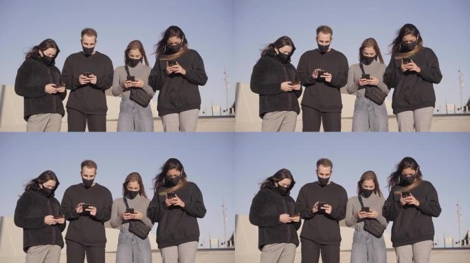 一群戴着口罩的朋友使用智能手机。新型冠状病毒肺炎季节新的正常生活方式。