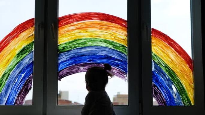 小女孩的背景画彩虹在窗户上。孩子们在家休闲。在家中隔离大流行冠状病毒Covid-19期间，积极的视觉