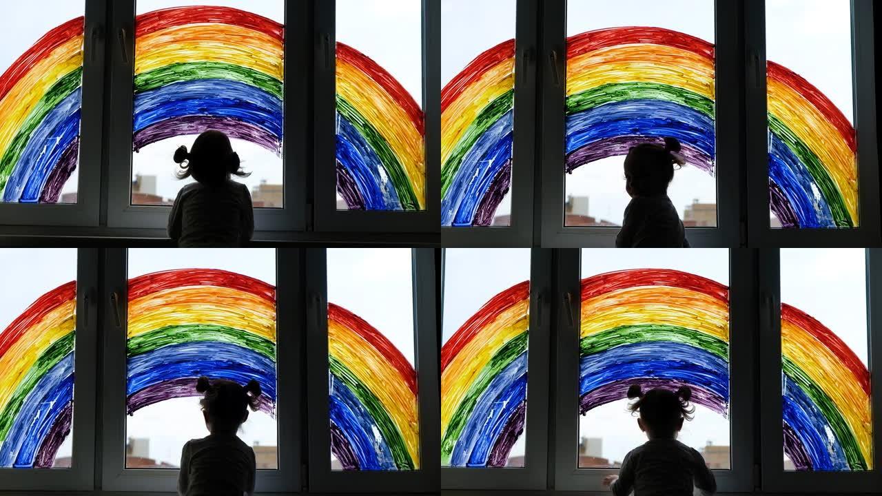 小女孩的背景画彩虹在窗户上。孩子们在家休闲。在家中隔离大流行冠状病毒Covid-19期间，积极的视觉