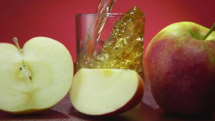将新鲜的苹果汁倒入慢动作的红色背景上的玻璃杯中