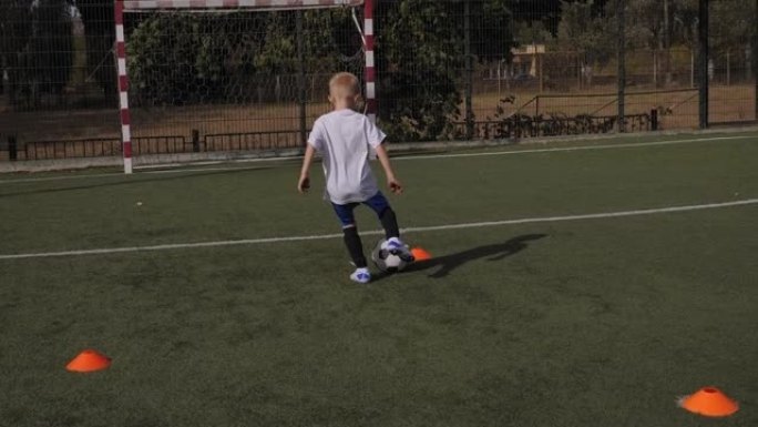 一个小男孩在足球场上训练，他练习运球和射门。