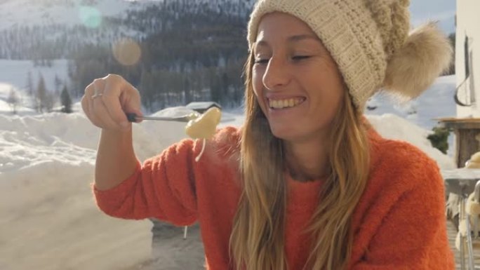 快乐的年轻女子在瑞士吃奶酪火锅，在冬季假期享受阿尔卑斯山和白雪皑皑的山脉。人们饮食传统当地观念