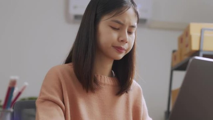 疲倦的年轻亚洲妇女使用笔记本电脑，长时间工作后在家庭办公室感到眼睛疲劳。