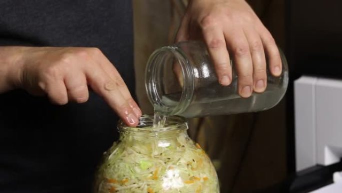 一个人将水和盐倒入一罐切碎的白菜中。用手指密封。大流行期间在家泡菜。特写镜头。
